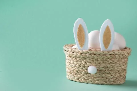 A basket with rabbit ears, in which Easter eggs lie on a light blue background Stock Photos