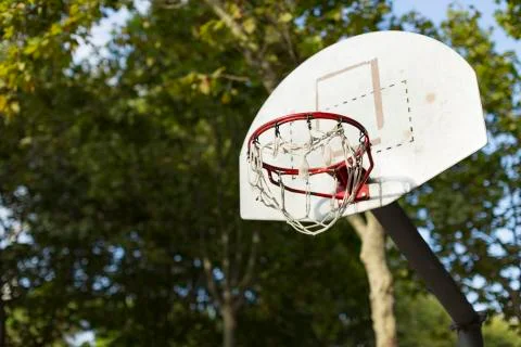 Basketball hoop in sunlight in a park with trees in the background Stock Photos