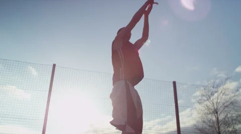 Basketball player dribbles the ball and takes a jump shot in the sunlight Stock Footage