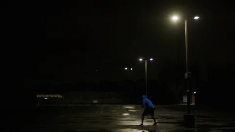 Basketball player dribbling the ball in an empty car park at night under a stree Stock Footage 115725393