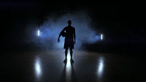 Basketball player knocks the ball in the light of the lamps shining behind Video stock 100310674