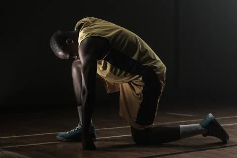 Basketball player preparing to play with knee on the floor and head lowered Stock Photos