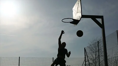 Basketball player silhouette slam dunking the ball outdoors Stock Footage