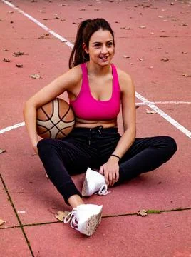 The basketball player is sitting down while holding the ball with her arm Stock Photos