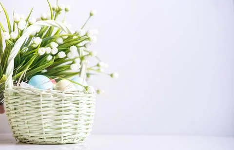 Baskets with Easter colored eggs on a white wooden table surrounded by delicate Stock Photos