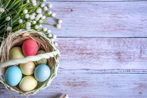 Baskets with Easter colored eggs on a white wooden table surrounded by delicate Stock Photos