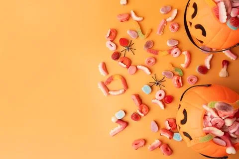 Baskets in the form of pumpkins with sweets and spiders on an orange background Stock Photos