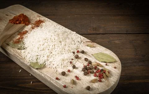 Basmati rice scattered on the kitchen table, spices on the cutting board Foto stock