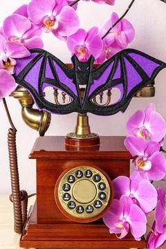 Bat shaped mask on old-fashioned phone with orchid flowers Stock Photos