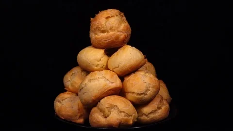 Batch of ruddy eclairs, put in pyramid on plate, rotating on black background Stock Footage 74884248