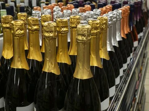The batch of sparkling wine bottles stand in a row on the wine store shelf. Stock Photos
