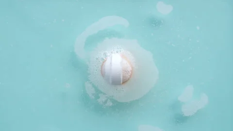 Bath bomb ball in blue background dissolves in water with white foam bubbles Stock Footage 256481072