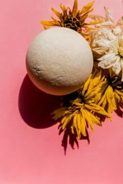 Bath bomb with a rough texture on a background of buds. Pink background. Stock Photos