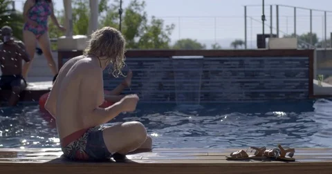 Bather jumps into swimming pool behind relaxed guy in sunglasses 4K Stock Footage 79735178