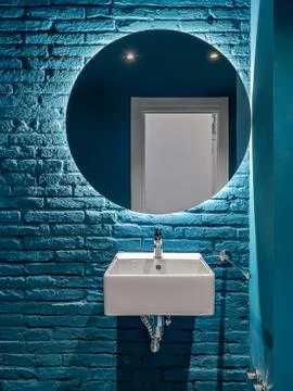Bathroom with blue bricks wall, square wash basin and round mirror. Minimalist Stock Photos