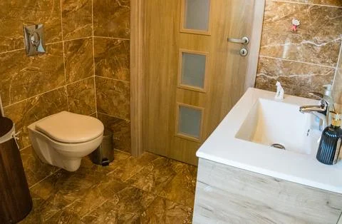Bathroom with brown tile wall trim, bamboo basket and white toilet and washbasin Stock Photos