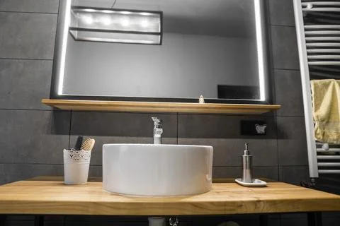 Bathroom interior with grey tile on a wall, stylish round sink and tap on a oak Stock Photos