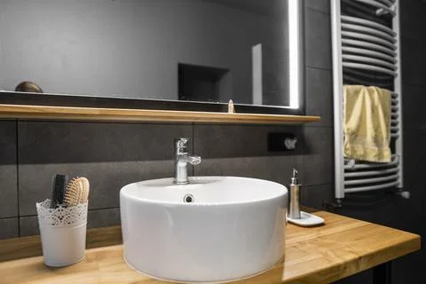Bathroom interior with grey tile on a wall, stylish round sink and tap on a oak Stock Photos