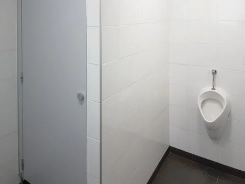 The bathroom interior is lined with white ceramic tiles. Oval ceramic urinal. Stock Photos