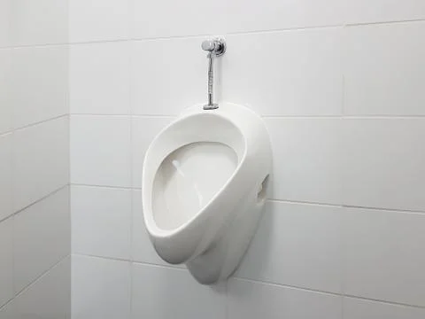 The bathroom interior is lined with white ceramic tiles. Oval ceramic urinal. Stock Photos