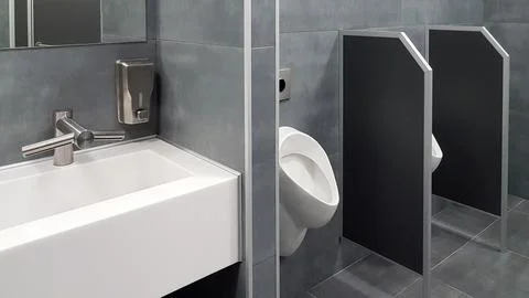 The bathroom interior is lined with white ceramic tiles. Oval ceramic urina.. Stock Photos