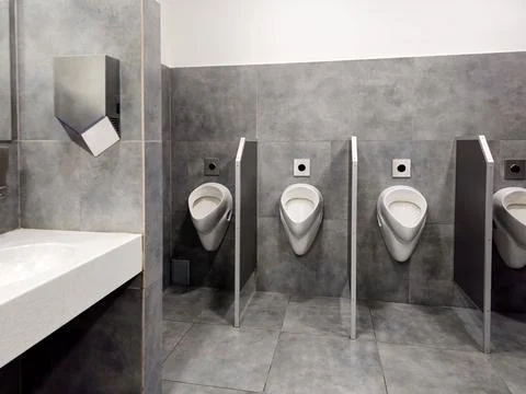 The bathroom interior is lined with white ceramic tiles. Oval ceramic urina.. Stock Photos