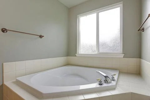 Bathroom nook features white corner tub under the window with white tiled tub Stock Photos