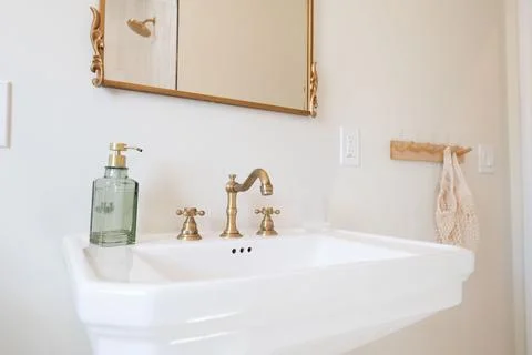 Bathroom sink featuring a white basin, brass faucet, and elegant details. T.. 스톡 사진