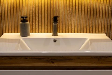A bathroom space features a white sink with a wooden base. A soap dispenser.. Stock Photos