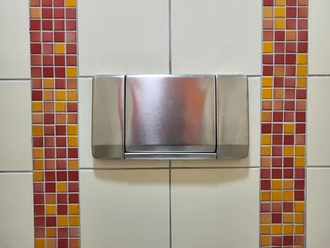 In the bathroom, there is a large flush button on the tile wall. Stock Photos