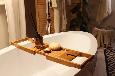 Bathtub with reed diffuser, loofah and burning candle in dark room Stock Photos