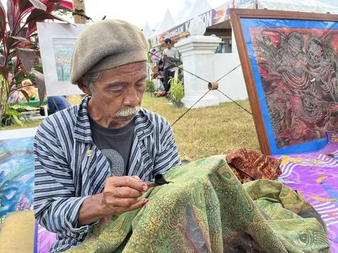 Batik drawing process by an old man on a fabric. Stock Photos