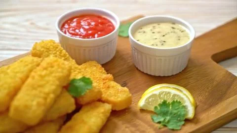 Battered fish fillets with lemon and dipping sauces on a wooden board Stock Photos