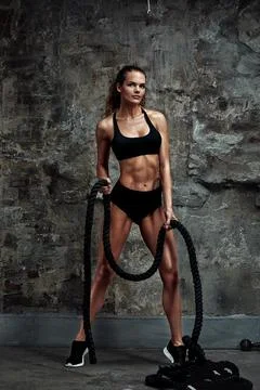 Battle ropes session. Attractive young fit and toned sportswoman working out in Stock Photos