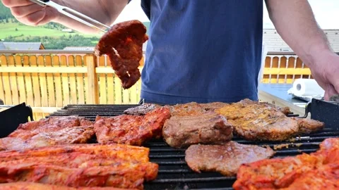 BBQ and Grill.man in a blue T-shirt turns grilled meat with a long fork. Stock Footage 256492453