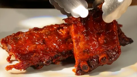 BBQ ribs steaming hot on plate. Seperating with tongs cu B Video stock 106828042
