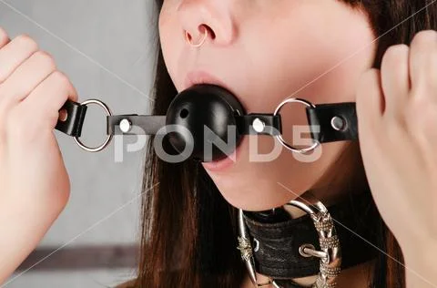 BDSM outfit for adult sex games. A young woman with a collar holds a gag in h Stock Photos