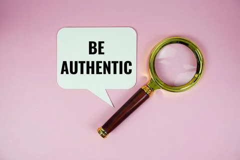 Be authenic text on speech bluble with magnifying glass top view on pink ba.. Stock Photos