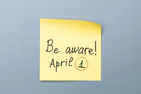 Be aware on yellow sticky note over a grey background. april fools day Stock Photos