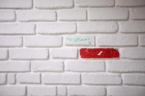 "Be Different" written on a white brick wall with single red brick Stock Photos