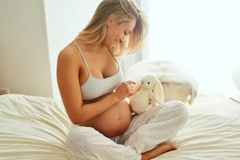 Be a good bunny to my baby. a pregnant woman holding a stuffed toy while sitting Stock Photos