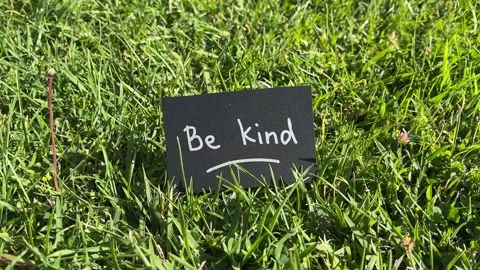 Be kind - black note with motivational text on the grass in the background Video stock 339510394