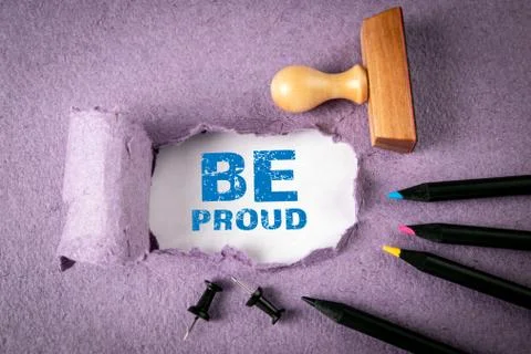 BE PROUD concept. Text under torn paper. Pencils and office supplies Stock Photos
