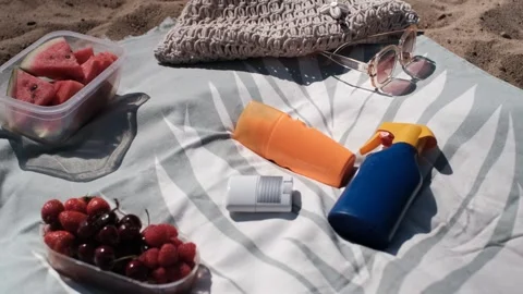 Beach accessories on a towel: sunscreen, fruit, sunglasses, woven bag 스톡 동영상 313290857