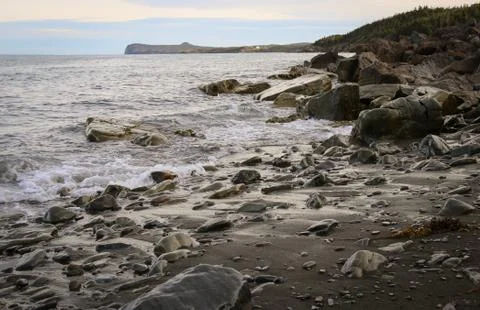 Beach and rocks with waves rolling across rugged landscape Stock Photos