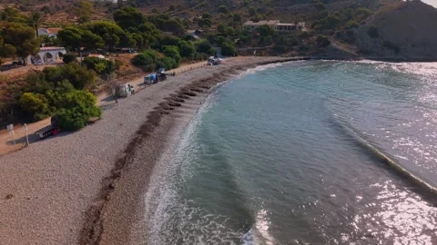Beach area with calm waves and pebbled shore near hills and homes during sunny Stock Footage 342787752