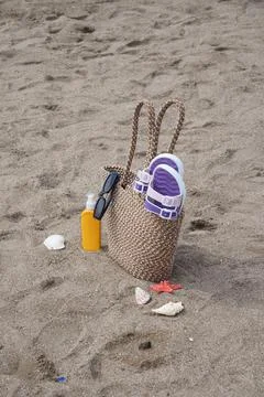 Beach bag sits on sand with sunscreen and shells Stock Photos