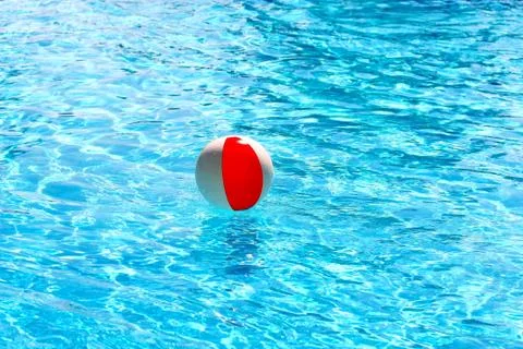 Beach ball floating in a pool with small waves reflecting in summer sun Stock Photos