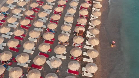 Beach beds and rows of thatch umbrellas - tiki straw parasols by the sea Stock Footage 212977740