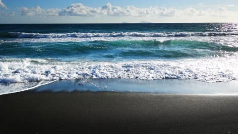 Beach with black volcanic sand and the blue sea at sunset. Stock Footage 255636697